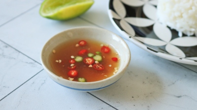 A small bowl of nam pla prik next to a lime and scoop of rice.