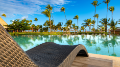 a chaise lounge overlooking a pool at a resort with palm trees in background