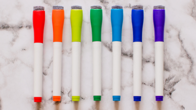 A line of dry erase markers in a rainbow of colors lying on a countertop