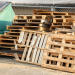 Stack of wood shipping pallets with beside a garbage dumpster