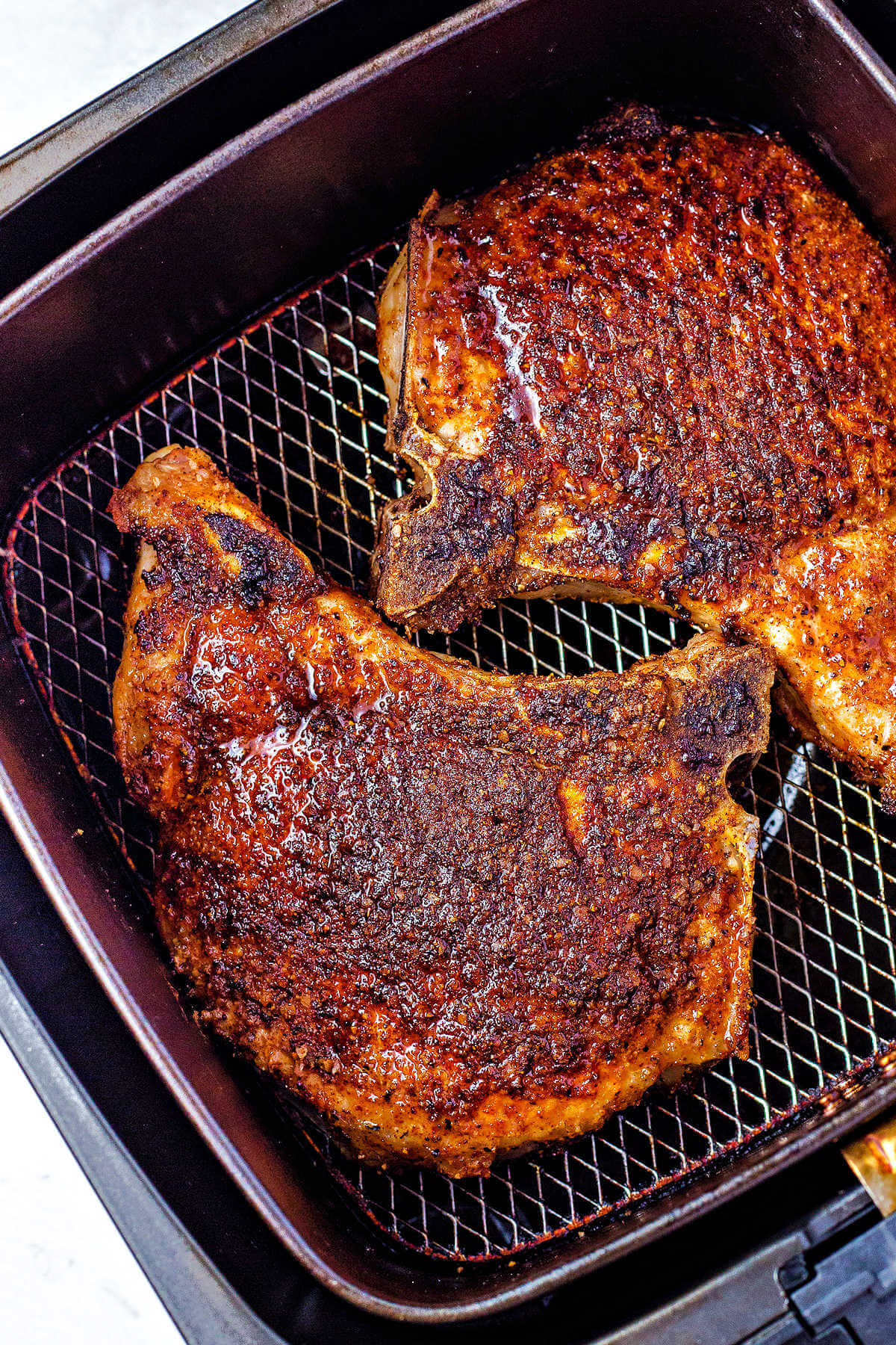 cooked and seasoned pork chops in an air fryer basket.