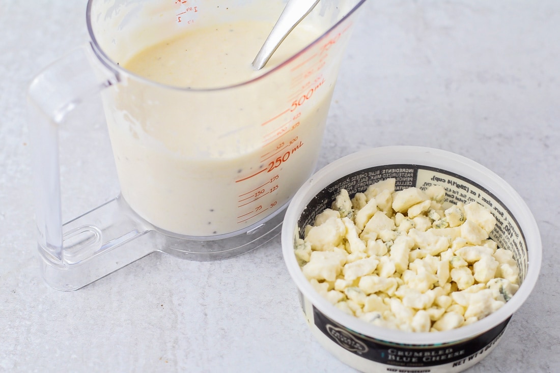 Wedge salad dressing in a measuring cup, with bleu cheese crumbles on the side.