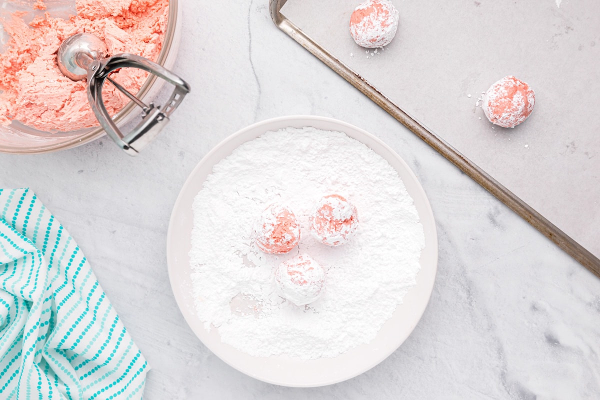 Balls of strawberry cake mix cookie dough dipped and rolled in powdered sugar.