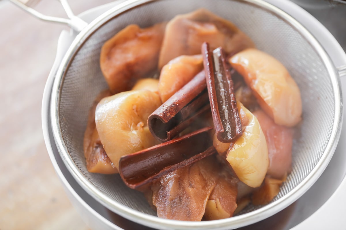 Cooked apples and cinnamon sticks in a colander.