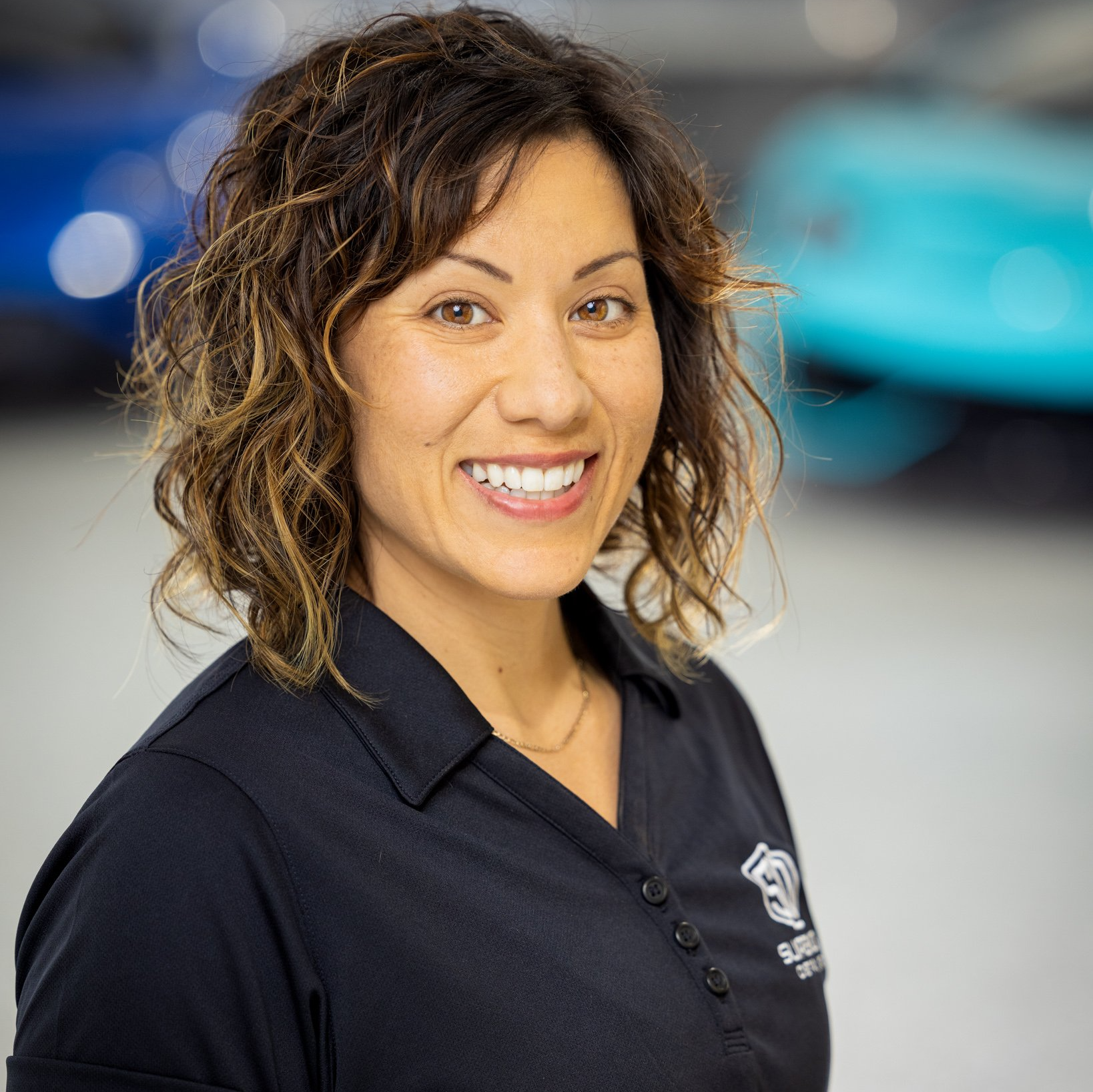 A woman in a black shirt is smiling in front of a blue car.