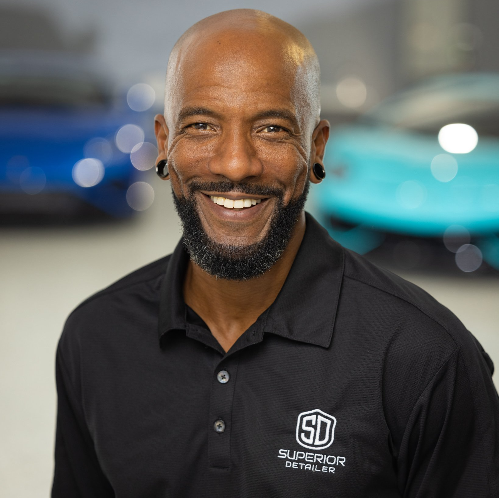 A man with a beard is smiling in front of a blue car.