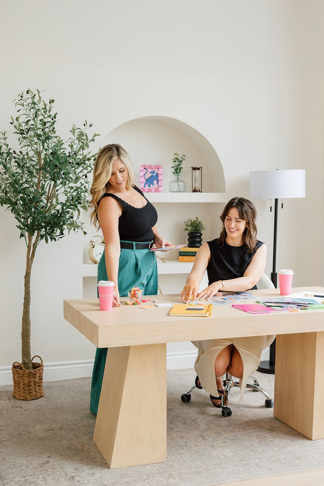 Two women are standing next to each other at a desk.