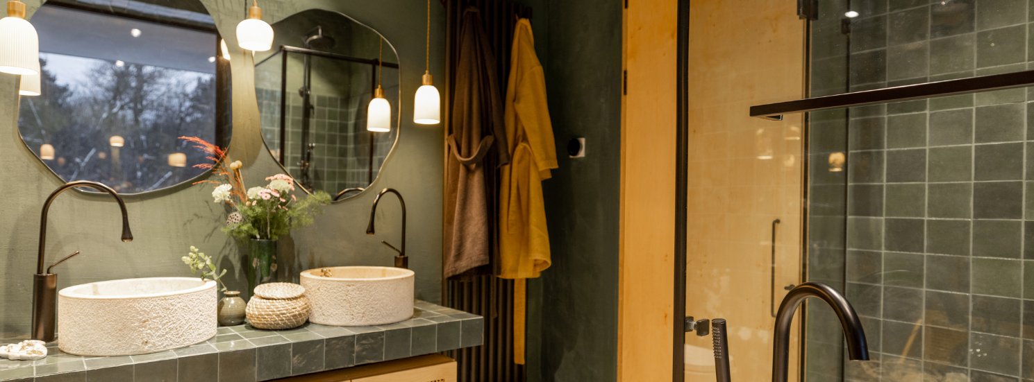 A bathroom with two sinks , a mirror, a shower and green tiles. 