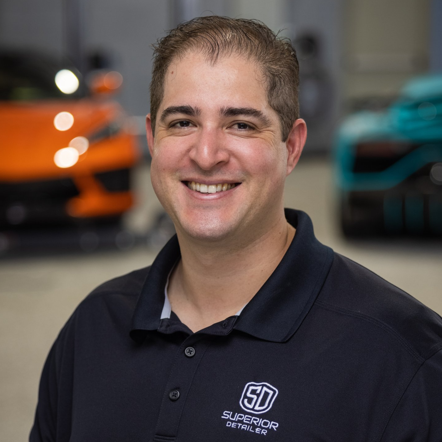 A man in a black shirt is smiling in front of a car.