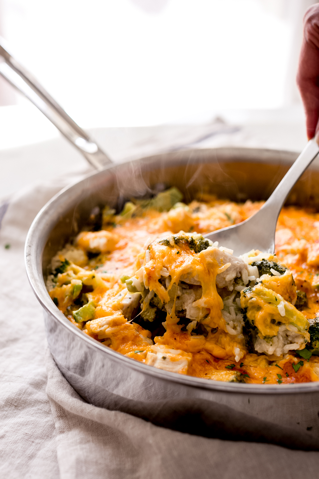 lifting a spoonful of casserole with melted cheese and broccoli showing