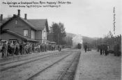 1931: Tog 361 kjører som det første normalsporede toget inn på Koppang stasjon med en stor folkemengde på plattformen. En vogn i smalsportoget som skal videre nordover til høyre.