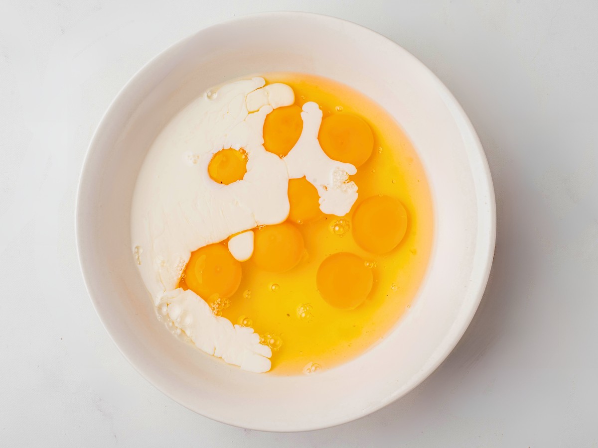 cracking eggs and mixing with heavy cream in a bowl.