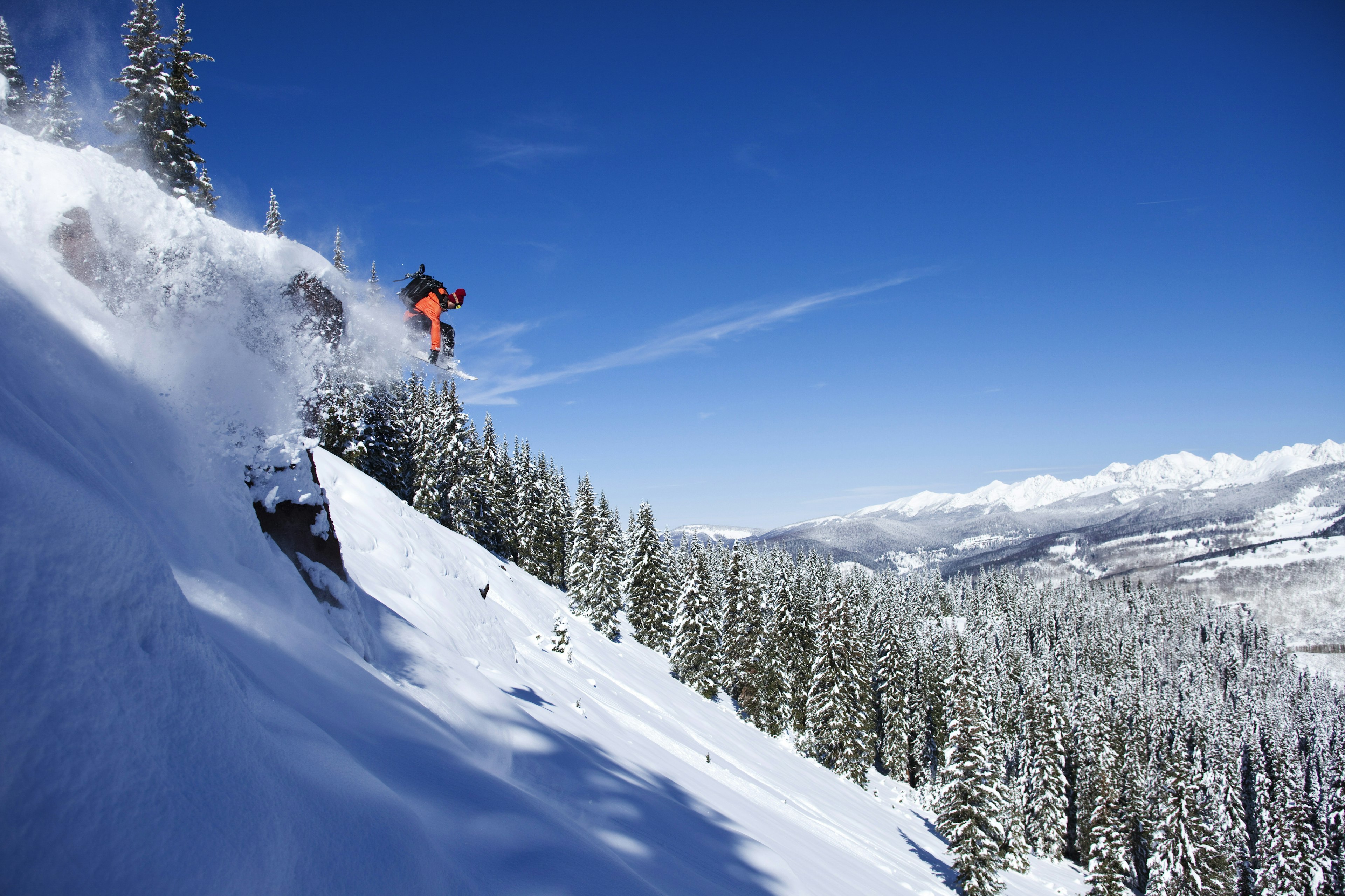 A athletic snowboarder jumping off a cliff on a sunny powder day