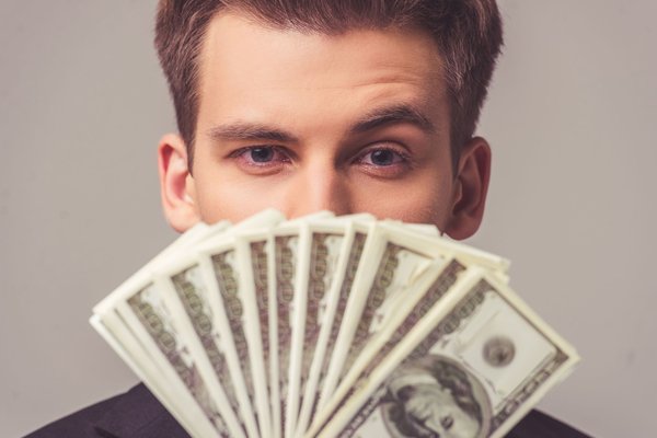 Person holding dollar bills up under their eyes.