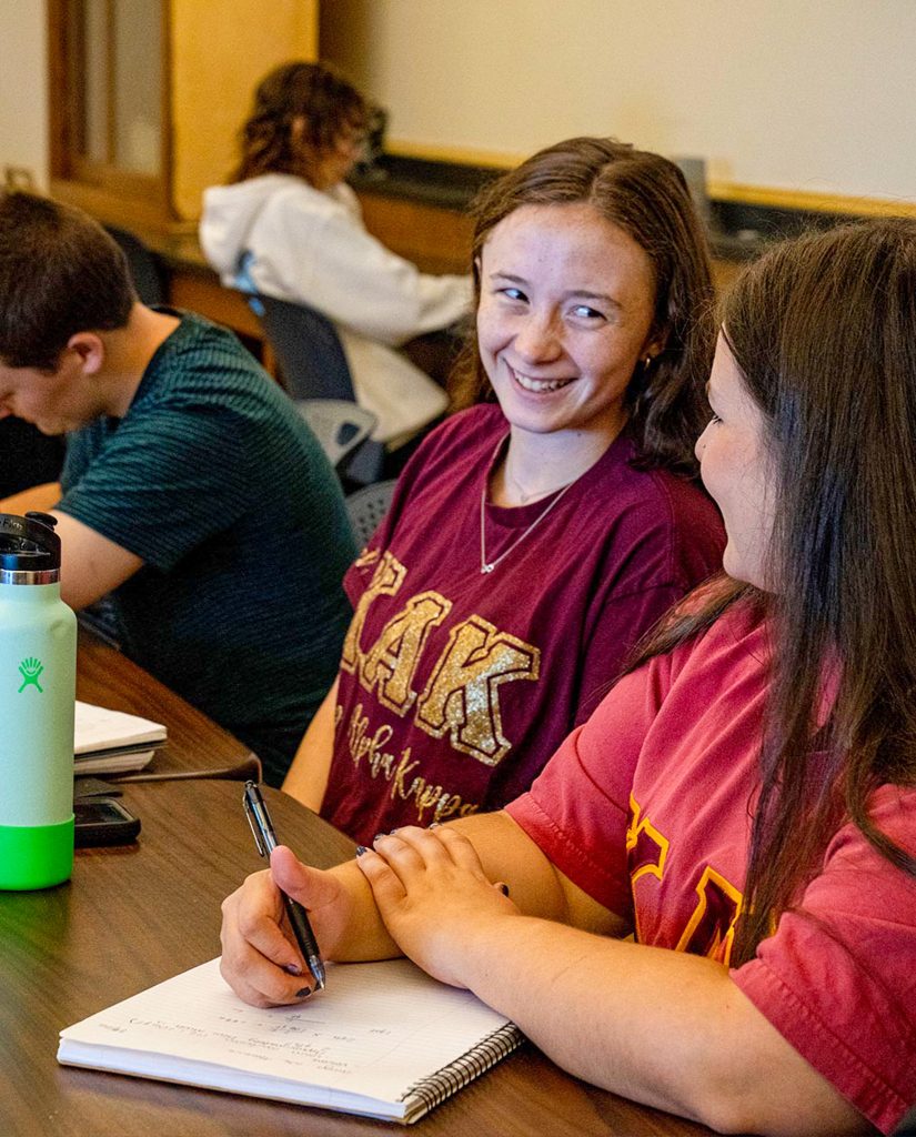 Machias students smiling while taking notes in class