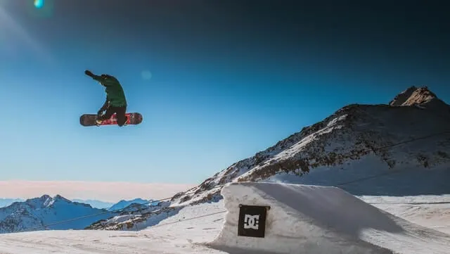 Snowboarder in mid air after taking off from a snowboard ramp with crisp white snow and clea blue sky backdrop