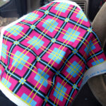 A square of brightly coloured plaid spandex being held up in front of a steering wheel.