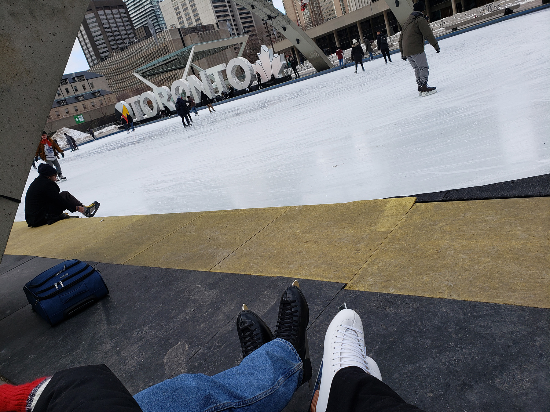 Two pairs of skate-clad feet in front of the rink at Nathan Phillips Square.