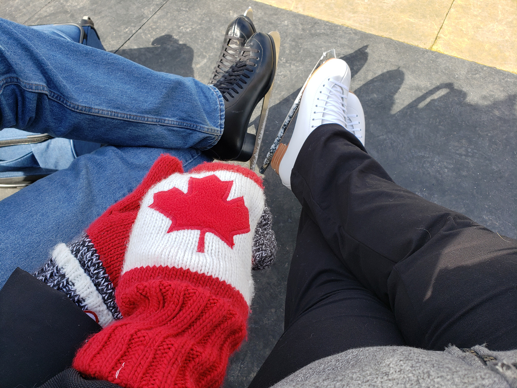 Two sets of crossed legs wearing figure skates, hands held in the foreground.