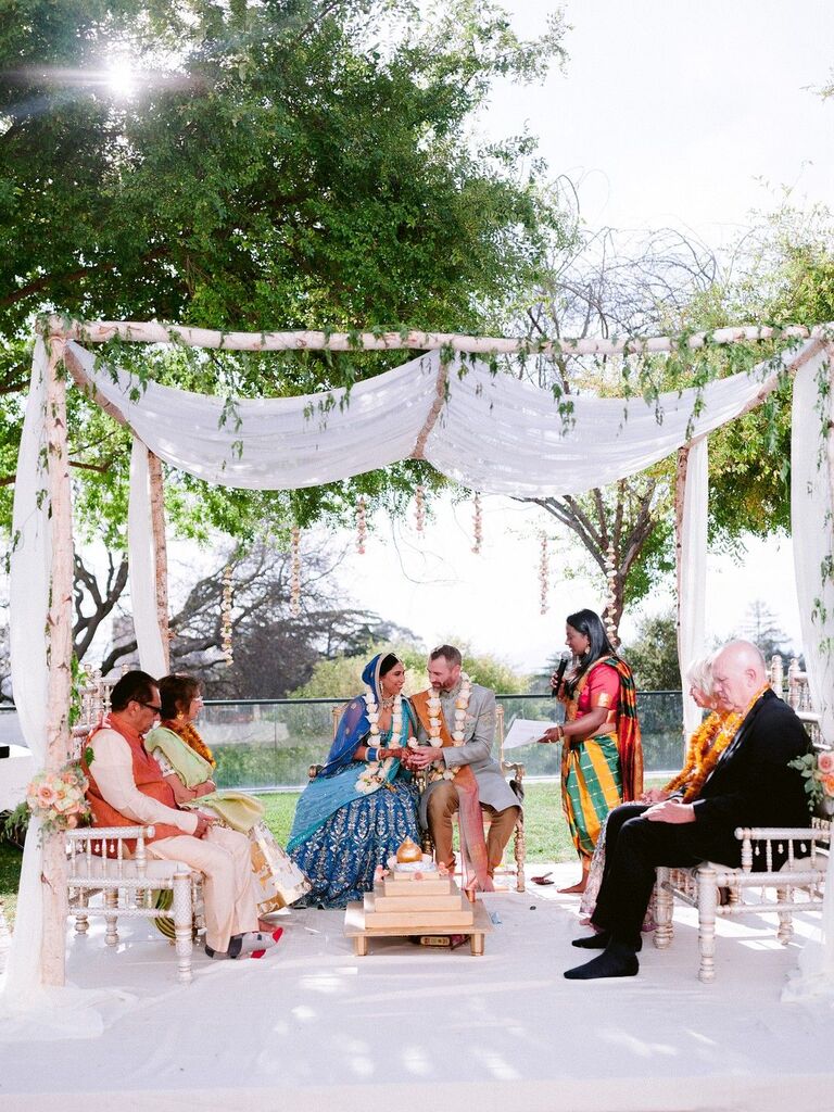 Couple and parents underneath simple wood mandap