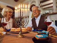 Older couple smiling and drinking wine at dinner table with lit menorah 