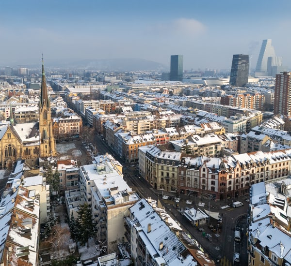 Stadtansicht von Basel im Winter mit schneebedeckten Dächern und Kirche.",