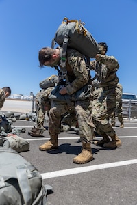 U.S. Army Soldiers with 301st Tactical Psychological Operations, PSYOP, Company (Airborne),14th PSYOP Battalion, 7th PSYOP Group, assist each other with their static-line chutes before performing pre-jump checks during a U.S. Air Force KC-130 Hercules static-line jump exercise at Naval Base Coronado, California, June 11, 2021. The 301st TCP invited I Marine Expeditionary Force Information Group PSYOP Marines to observe jump training before attending the U.S. Army Airborne school. Gaining jump qualifications enables I MIG to effectively integrate and support I Marine Expeditionary Force information operations in forward deployed environments.