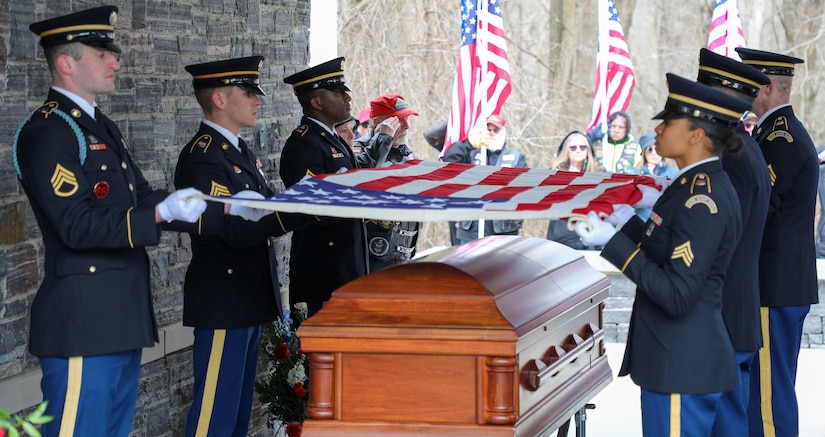 National Guardsmen hold the American flag above a casket while a crowd watches on.