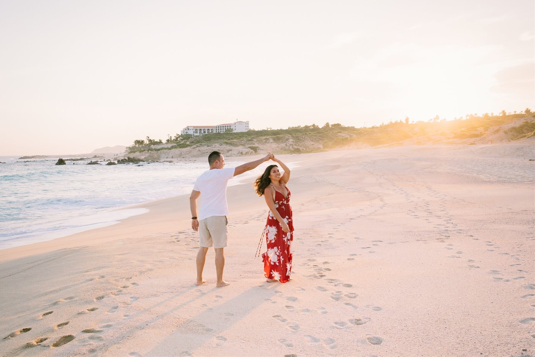 A man and woman dance in the sand on a beach at sunset in Cabo San Lucas