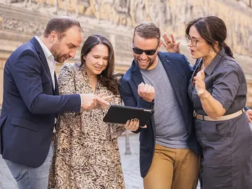 Vier Personen schauen zusammen auf ein Tablet und lachen.