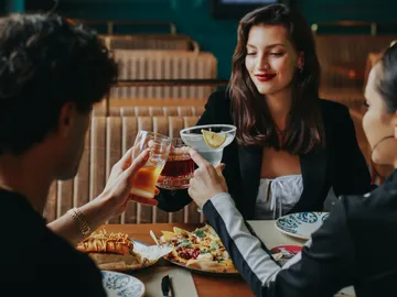 Drei Personen stoßen mit Getränken in einem Restaurant an.