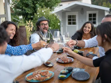 Freunde stoßen mit Gläsern an, draußen am Tisch.