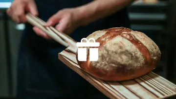 Bäcker hebt frisch gebackenes Brot mit Holzschaufel an.