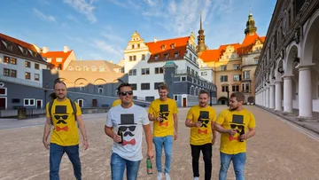 Sechs Männer in T-Shirts spazieren durch eine historische Stadt.