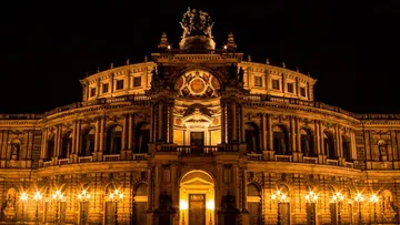 Historisches Gebäude erleuchtet nachts, umgeben von Straßenlaternen.