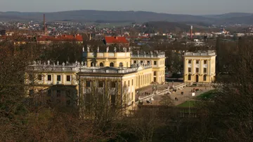 Historisches Gebäude steht, Menschen spazieren im Park.