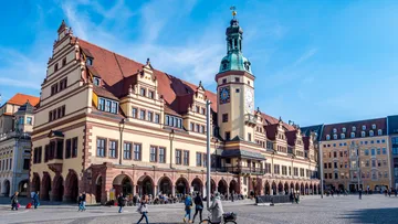 Historisches Gebäude mit Turm, Menschen im Freien, sonniger Platz.