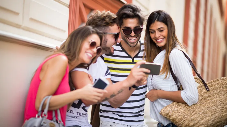 Vier Freunde schauen gemeinsam auf ein Handy in der Stadt.