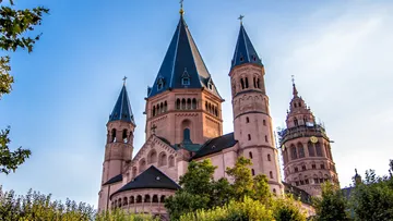 Fassade einer Kirche mit Türmen, umgeben von Bäumen.