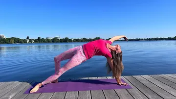 Frau macht Yoga auf einem Steg am Wasser.