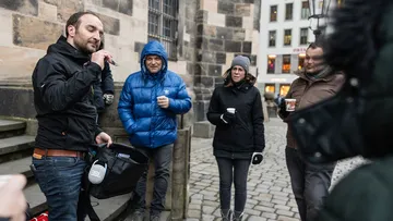 Fünf Menschen stehen draußen und hören einer Erklärung zu.