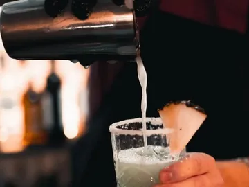 Cocktail wird aus Shaker in Glas gegossen, fruchtig dekoriert.