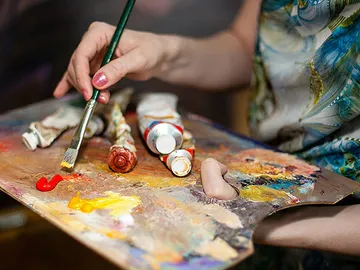 Pinsel mischt Farben auf einer Künstlerpalette in einem Atelier.