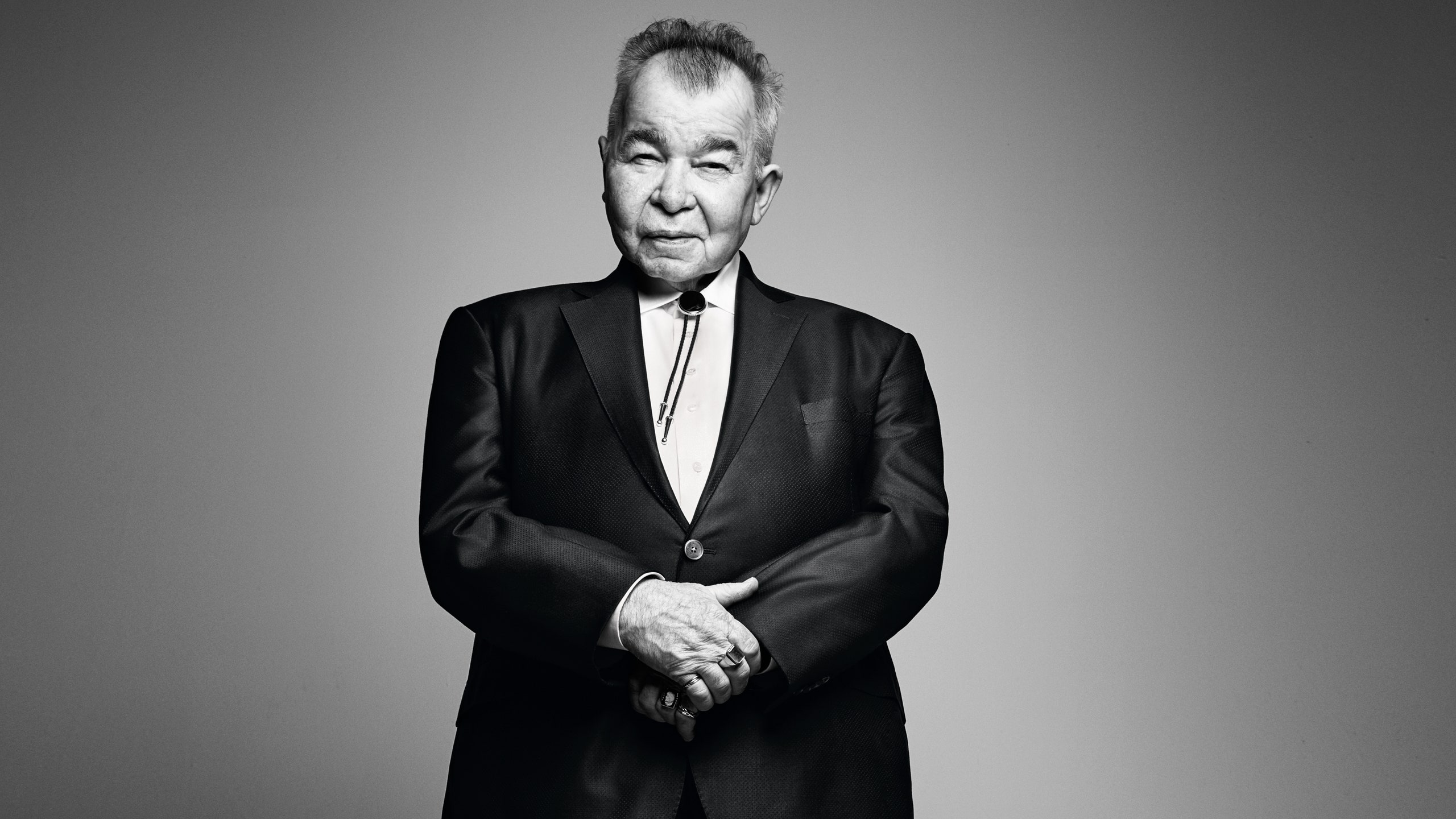 This image may contain John Prine Coat Clothing Overcoat Apparel Suit Human Person Standing Man and Tie