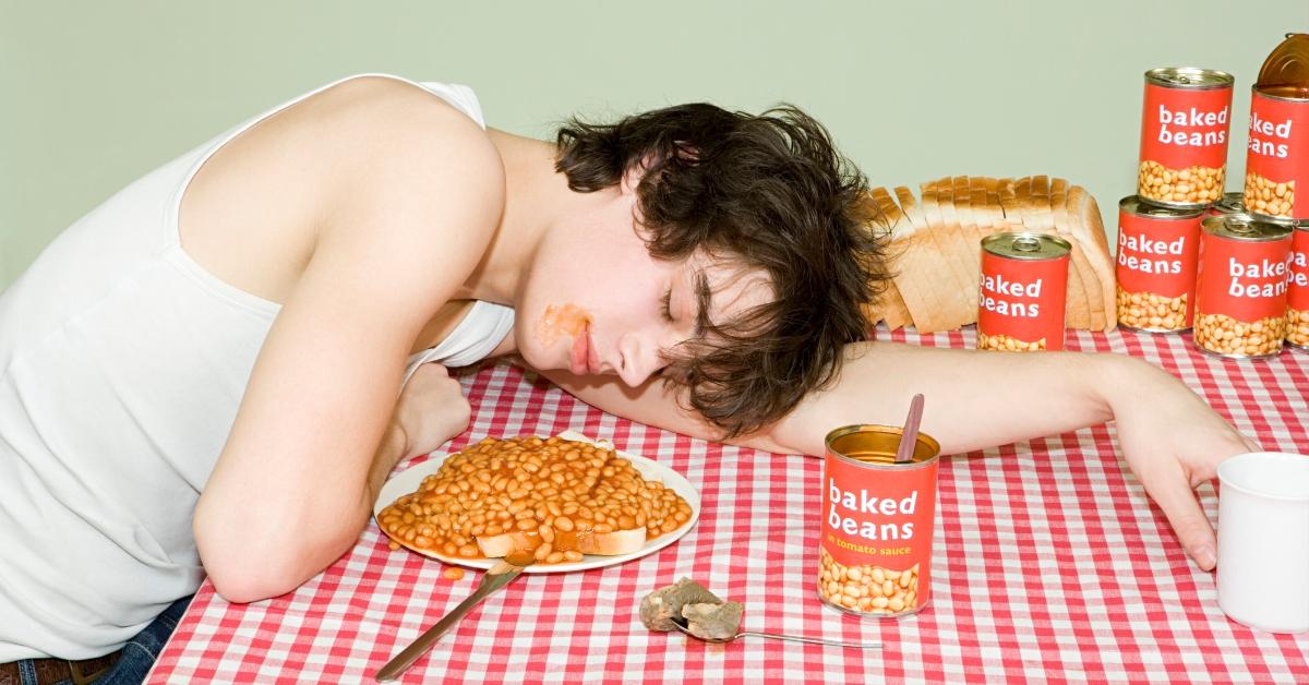 A man resting surrounded by baked beans. 