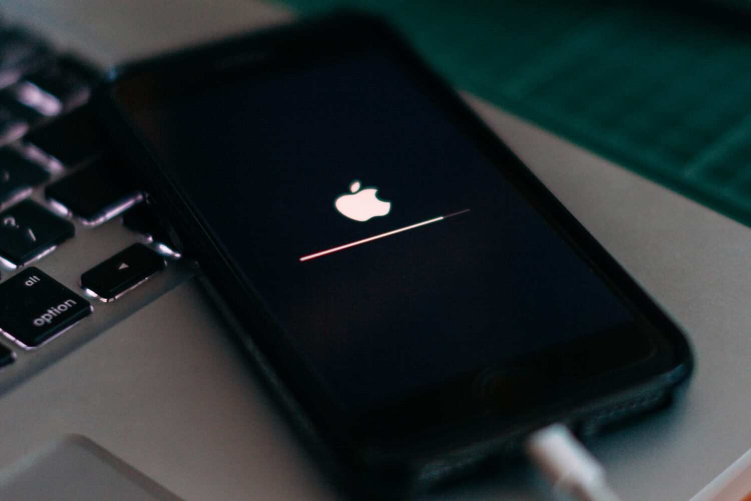 An iPhone laying on a MacBook, showing an iOS update progress bar