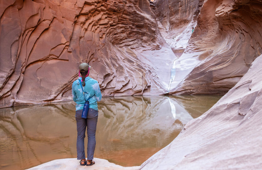 A woman stands at the edge of a large pool and looks at a trickling waterfall in a side canyon of Grand Canyon.