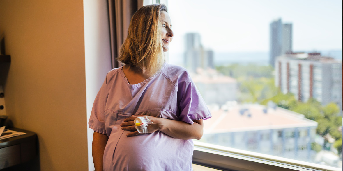 A pregnant woman looking out of the window of a private amenity room in an NHS hospital.