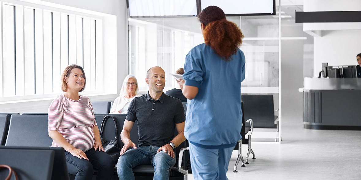 An expectant couple talking to a nurse in a hospital waiting room.