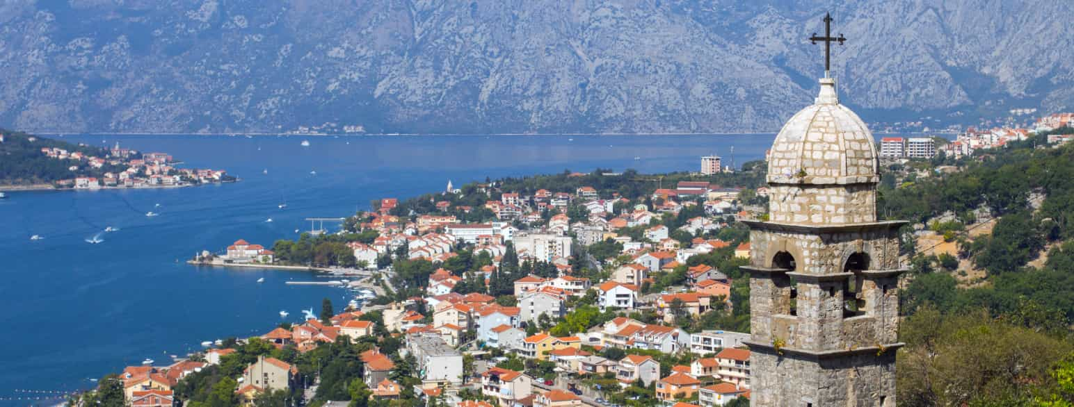 Bilde av Kotorbukta i Montenegro. I forgrunnen kan man se toppen av et kirketårn i stein og i bakgrunnen fjord og by. 